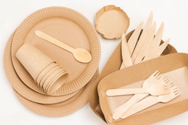 Tek kullanımlık karton tabaklar, tahta çatallar ve bıçaklar. Piknik için tek kullanımlık kağıt sofra takımı, fast food. Beyaz arka plan. Düz yatıyordu