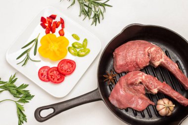 Kemikli dana eti, sarımsak ve tavada yıldız anason. Beyaz tabakta dilimlenmiş domates ve biber. Biberiye ve maydanoz karışımı. Beyaz arka plan. Düz yatıyordu