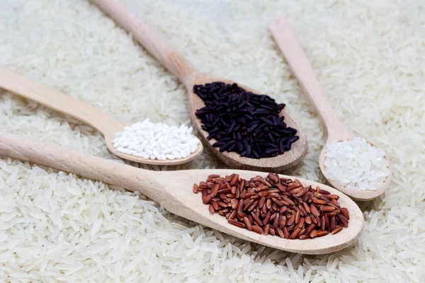 Red rice, glutinous rice, black basmati rice in wooden spoons. Basmati rice is scattered as food background. Close up. Top view