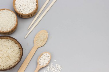 Hindistan cevizi kabuklu Basmati pilavı. Yuvarlak ve ahşap kaselerde beyaz pirinç. Bambu çubukları. Pirinçli tahta kaşıklar. Gri arka plan. Uzayı kopyala Düz yatıyordu