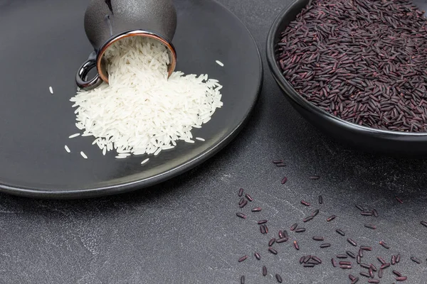 Siyah kasede siyah pirinç. Siyah tabakta beyaz basmati pilavı. Üst Manzara. Uzayı kopyala Siyah arkaplan
