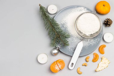 Dal dalları. Gri tabakta un olan elek. Mandalina ve mandalina dilimleri. Noel hala hayattır. Düz yatıyordu. Uzayı kopyala Gri arkaplan