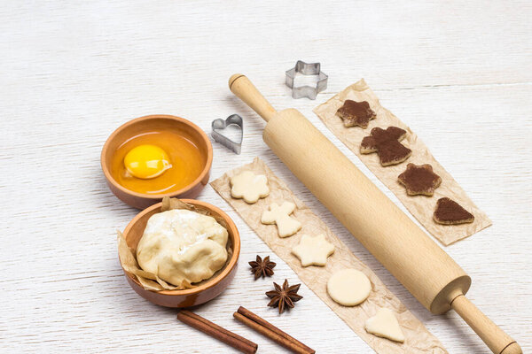 Cutting shaped cookies by mold sprinkled with chocolate on paper. Eggs, Dough, cinnamon sticks and rolling pin. Top view. White Background