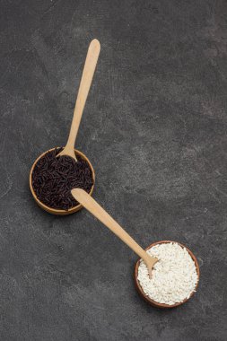 Tahta kasede siyah beyaz pirinç. Tahta kaşıklar kasede. Uzayı kopyala Düz yatıyordu. Siyah arkaplan