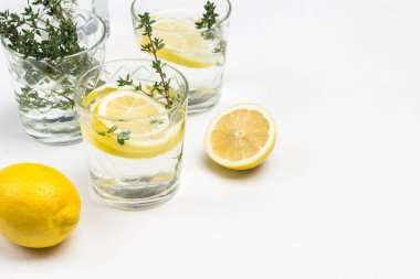 Bardakta limon. Camda kekik filizleri var. Limonlar masada ve seramik kasede. Kapatın. Beyaz arka plan. Üst görünüm