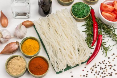 Pirinç eriştesi ve kuru baharatlar yeşil küçük kaselerde. Soğan, biberiye filizi. Cam şişede soya sosu. Üst Manzara. Beyaz arkaplan