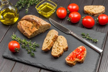 Ekmek ve bıçak parçaları. Domatesli sandviç. Domates, zeytinyağı, kekik filizi. Parti başlangıcı ya da aperatif. Karanlık Ahşap Arkaplan. Üst görünüm