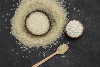 Tahta kaselerde ve kaşıkta beyaz pirinç. Pirinç masaya saçıldı. Uzayı kopyala Siyah arka plan. Düz yatıyordu