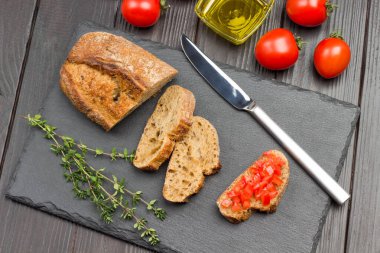 Ekmek ve bıçak parçaları. Domatesli sandviç. Domates, zeytinyağı, kekik filizi. Parti başlangıcı ya da aperatif. Karanlık Ahşap Arkaplan. Üst görünüm