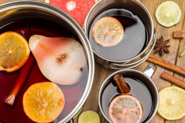 Turunçgiller, metal bardak ve tencerelerde baharatlı şaraplar pişirir. Yıldız anason, portakal dilimleri ve tarçın çubukları masada. Düz yatıyordu