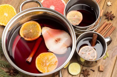 Turunçgiller, metal bardak ve tencerelerde baharatlı şaraplar pişirir. Yıldız anason, portakal dilimleri ve tarçın çubukları masada. Ahşap arkaplan