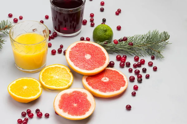 Cranberry and orange drinks in glasses. Slices of orange, grapefruit and cranberries, sprigs of fir on table. Grey background. Top view