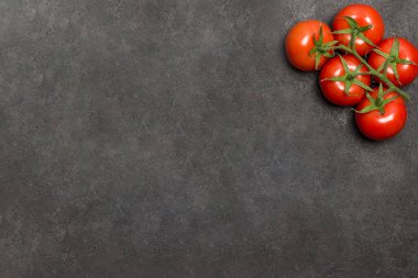 Çerçevenin köşesindeki yeşil dalda kırmızı domatesler. Siyah arka plan. Düz yatıyordu. Boşluğu kopyala