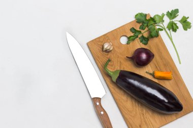 Eggplant and onion on cutting board. Sprig of parsley and kitchen knife on table. White background. Flat lay. Copy space