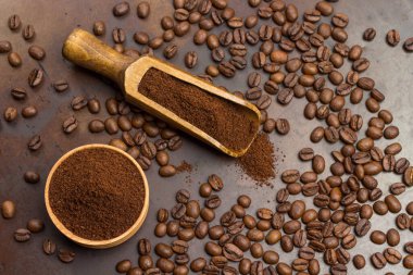 Tahta kasede ve kepçeyle öğütülmüş kahve. Kavrulmuş kahve çekirdekleri masada. Paslı metal arka plan. Düz yatıyordu