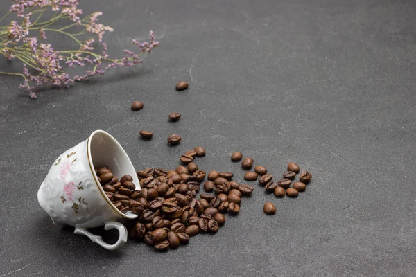 Kavrulmuş kahve çekirdekleri fincandan masaya saçılmıştır. Siyah arka plan. Boşluğu kopyala
