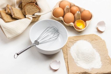 Kasede çırpın. Kağıt üzerinde un. Karton kutuda yumurtalar. Beyaz peçetede tost. Beyaz arkaplan. 