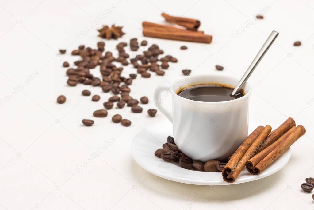 Cinnamon sticks and coffee grains on white saucer. Coffee drink in white cup. Grains of coffee on table. White background. Copy space
