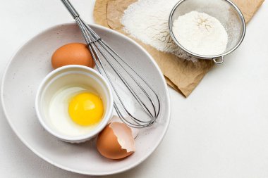 Yumurta sarısı küçük kasede. Tavuk yumurtası, yumurta kabuğu ve büyük beyaz kasede çırpma. Kağıt üzerinde un ve elek. Beyaz arka plan. Düz yatıyordu