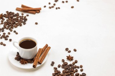 Bir fincan kahve, tarçın çubukları ve çay tabağında yıldız anason. Masada kahve ve tarçın taneleri var. Beyaz arka plan. Üst Manzara. Boşluğu kopyala