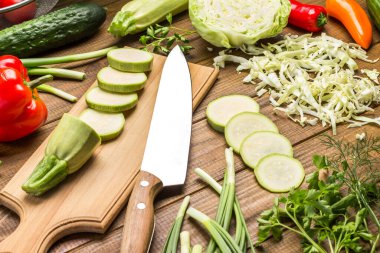 Mutfak bıçağı ve balkabağı kesme tahtasının üzerinde. Masada dilimlenmiş kabak ve lahana. Ahşap arka plan. Üst görünüm