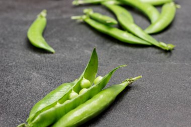 Opened pods of green peas and pods of green peas on table. Black background. Flat lay
