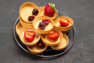 Kirazlı ve çilekli turtalar. Siyah arka plan. Üst görünüm