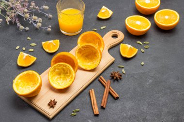 Kesme tahtasındaki portakal kabuğu. Tarçın çubukları ve bir bardak portakal suyu. Siyah arka plan. Üst görünüm