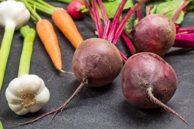 Üstü açık iki pancar kafası. Kapatın. Saplı ve havuçlu sarımsak. Siyah arka plan. Üst görünüm
