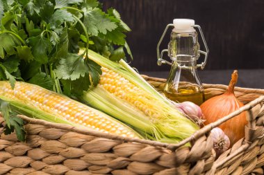 Taze mısır koçanları, yeşil maydanoz şişedeki yağ ve sepetteki sarımsak. Kapatın. Siyah arkaplan. 