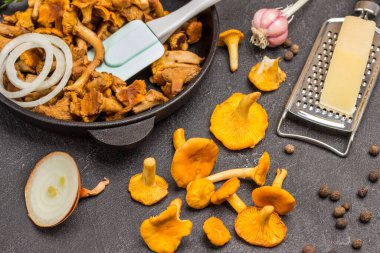 Çiğ mantarlar, şişede yağ ve masada peynir. Kızarmış mantar, spatula ve tavada doğranmış soğan. Siyah arkaplan