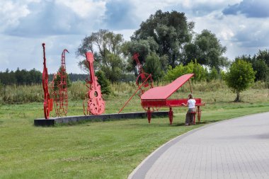 Park 'ta orkestra kurulumu, kırmızı piyano, çello ve keman. Kadın piyano çalmayı taklit ediyor. Doğanın arkaplanındaki soyut resim