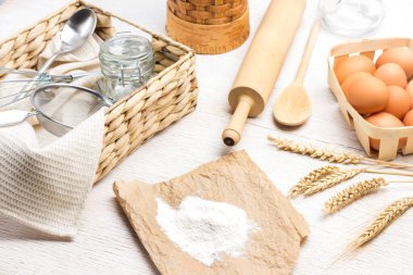 Kağıt üzerinde un. Buğday başakları. Hasır kutuda yumurtalar ve buğday başakları. Cam kavanoz, süzgeç ve kaşık sepeti. Beyaz arka plan. Üst görünüm