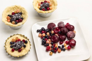 Donmuş böğürtlenlerden pasta yapmak. Pişirme kabında dışkı, tabakta böğürtlen. Beyaz arka plan. Üst görünüm