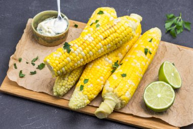 Tahtada haşlanmış mısır. Limon ve sos kasede. Maydanoz yaprakları. Siyah arka plan. Üst görünüm