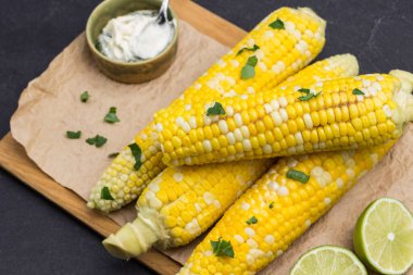 Tahtada haşlanmış mısır. Kasede sos. Maydanoz yaprakları. Siyah arka plan. Üst görünüm