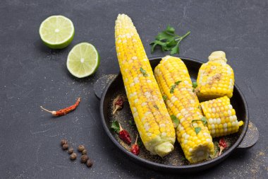 Kızartma tavasında haşlanmış mısır ve baharat. Masada limon ve kırmızı biber kabuğu var. Siyah arka plan. Üst görünüm