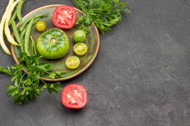 Tabakta kırmızı ve yeşil domates. Masada kırmızı domates ve maydanoz filizi var. Uzayı kopyala Siyah arka plan. Üst görünüm