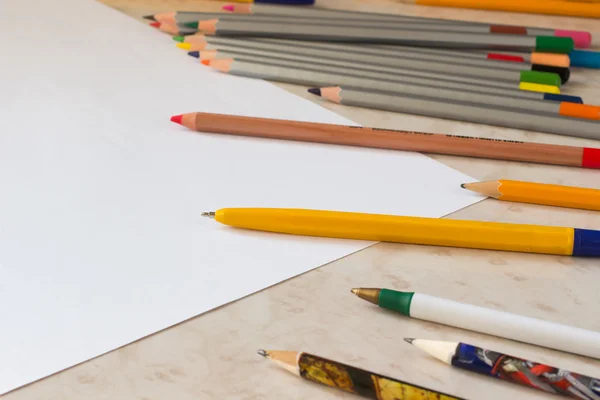 Colored pencils and white sheet of paper on the desk — Stock Photo, Image
