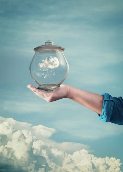 Рука держит стеклянную банку с голубым небом и облаками внутри — стоковое фото