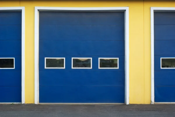 Blaue Garagentore an gelber Wand eines Geschäftshauses — Stockfoto