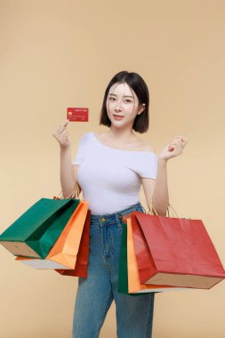 Mutlu genç Asyalı bir kadın renkli alışveriş çantaları ve kredi kartı taşıyor ve büyük bir satışın keyfini çıkarıyor. Perakende promosyonlar, indirim duyuruları ve e-ticaret reklamları için mükemmel..