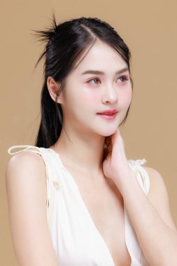 Uzun saçlı ve doğal makyajlı güzel bir Asyalı mankenin portresi. İzole edilmiş bej arka planda temiz, taze, parlak bir ten. Yüz bakımı, vücut bakımı, güzellik kliniği ve spa için ideal.