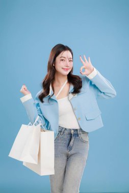 Bir sürü beyaz alışveriş torbası taşırken gülen mutlu genç Asyalı kadın. Başarılı ve eğlenceli bir alışveriş gününü temsil eden günlük kot pantolon ve tişört giyiyor..