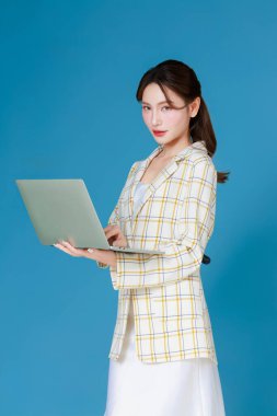 Diz üstü bilgisayar kullanarak sarı ekose ceket giyen zeki bir Asyalı kadının portresi. Modern ofis çalışanı, serbest çalışan, çevrimiçi pazarlamacı ve başarılı kadın girişimci kavramı.