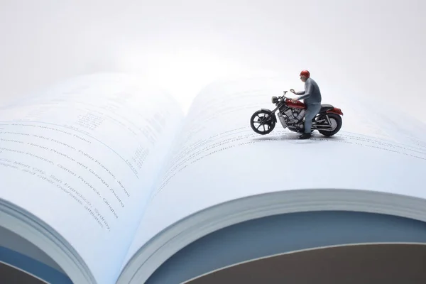 mini figure rides on a motorcycle over open diary book. Travel concept