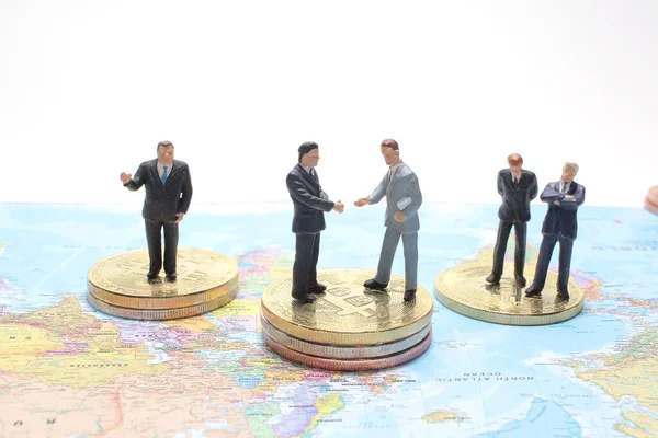 mini people: Businessman handshake with coins stack on world map