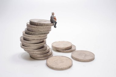 Adam minyatür figür fotokopi alanlarıyla dolu madeni paraların üzerinde oturuyor.