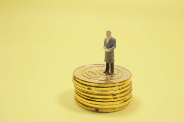 Bozuk para yığınının üzerinde duran minyatür bir adam.