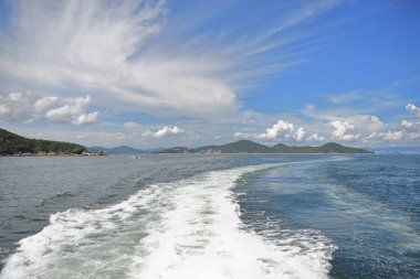 Denizdeki tekne yolu, sudaki beyaz köpük ve uzaktaki Hong Kong tepeleri.